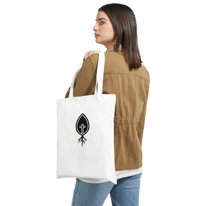 Woman wearing brown jacket holding Christian cross root logo canvas white tote bag