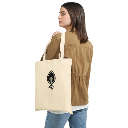 Woman holding natural canvas tote bag with black Christian cross and root logo